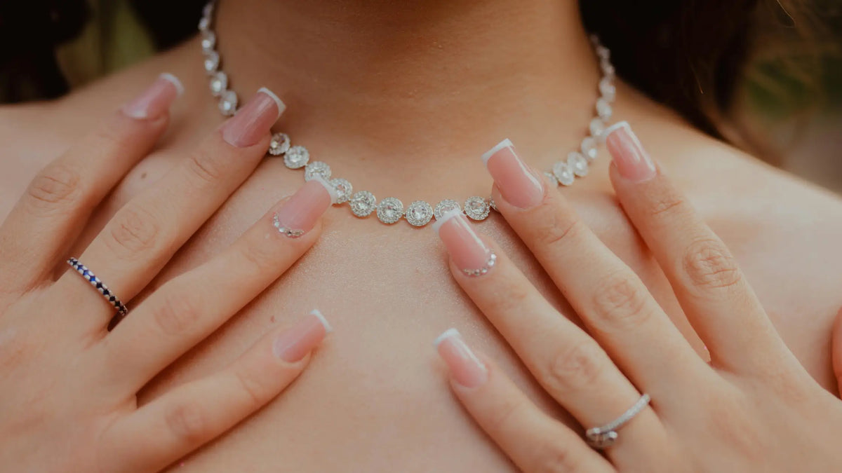 Close-up of a person wearing a diamond necklace with hands gently touching the chest.
